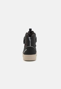 Chaussure montante noire avec une surface texturée, bande grise, sangle velcro et semelle crème. Comprend une languette et une marque au niveau du talon.