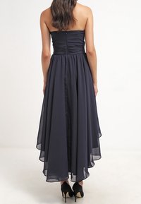 Ärmlös midnattsblå klänning med en åtsittande överdel och en flödande, asymmetrisk kjol. Slät tygtextur, dragkedjestängning bak, bärs med svarta klackar.
