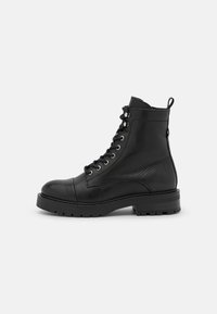 Bottines en cuir noir avec une pointe arrondie, un laçage, des œillets en métal et une semelle en caoutchouc durable avec un motif de grip texturé.