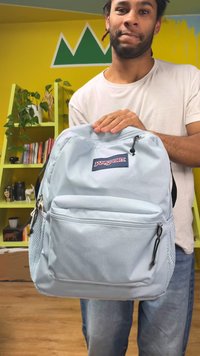 Lichtblauwe Jansport-rugzak met een textuur oppervlak, meerdere vakken, een voorvak met rits en zijvaknetten voor waterflessen.