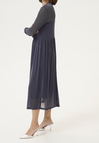 Mörkblå långärmad klänning med glittrande textur, samlad midja och flödande kjol. Matchad med silvriga klackskor.