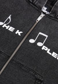 Zwarte zip-up hoodie met witte tekst en een muzieksleutelontwerp, gemaakt van zachte stof met een soepele ritssluiting en voorzakken.