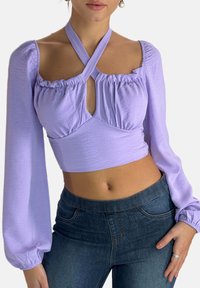 Haut court lavande avec manches longues bouffantes, détails froncés et une découpe en forme de trou de serrure au centre, fabriqué en tissu doux et texturé.