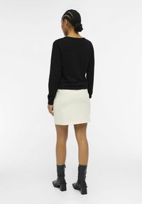 Suéter negro de manga larga y falda mini color crema combinada con botas de tacón negras; tejido de punto texturizado con un ajuste ceñido y escote redondeado.