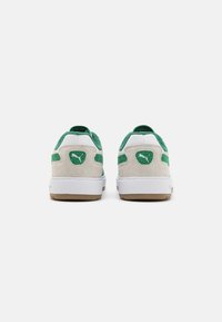 Zapatillas de ante beige con acentos verdes y una suela de goma blanca. Presenta un parche con el logo en el talón y superposiciones texturizadas.