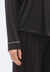 Mustast pika varrukaga rõivaese, millel on leplik lõige, valge ääris varrukaotstel, pehme kangas ja õrn läige, mis osaliselt katab kätt.