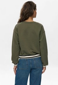 Felpa verde oliva con collo a giro, orlo a coste e dettagli a righe bianche e nere, abbinata a jeans blu a vita alta.