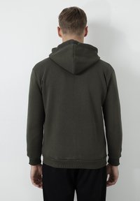 Sudadera de color verde oscuro con una tela texturizada, que presenta una capucha grande, puños acanalados y un ajuste relajado. La vista trasera muestra líneas limpias y un diseño sencillo.