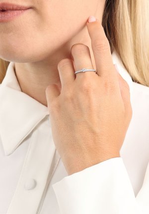 Anello d'argento con una piccola pietra centrale e una fascia texturizzata. Indossato su una mano con finitura naturale delle unghie, su uno sfondo di camicia bianca.
