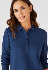 Marineblauw poloshirt met lange mouwen, gemaakt van zacht materiaal, met een klassieke kraag, een knoopsluiting met vier knopen en getailleerde mouwen.