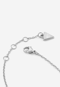 Bracciale in argento con maglie circolari, chiusura a moschettone e charm triangolare con inciso "GUESS". Texture liscia e finitura lucida.