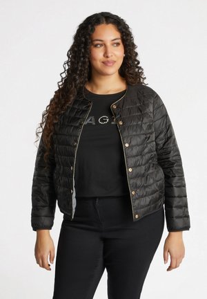 Black quilted jacket with a shiny finish, gold hardware buttons, and a fitted design. Worn over a black t-shirt with embellished text.