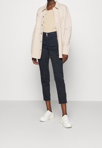 Krémová oversized bunda z vlněné směsi, béžový přiléhavý top, námořnické zúžené kalhoty se zipy, spárované s bílými teniskami. Minimalistický design a textura.