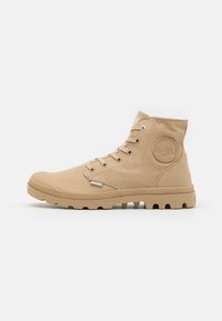 Stivaletti alti in tela beige con punta in gomma, chiusura con lacci e suola in gomma testurizzata, dotati di un patch rotondo del logo sul lato.