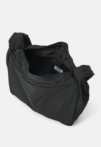 Zwarte nylon tas met een ritssluiting. Kenmerkt zich door een zachte, gestructureerde stof en een opvallend logo op de zijkant. Compact ontwerp met geknoopte handvatten.