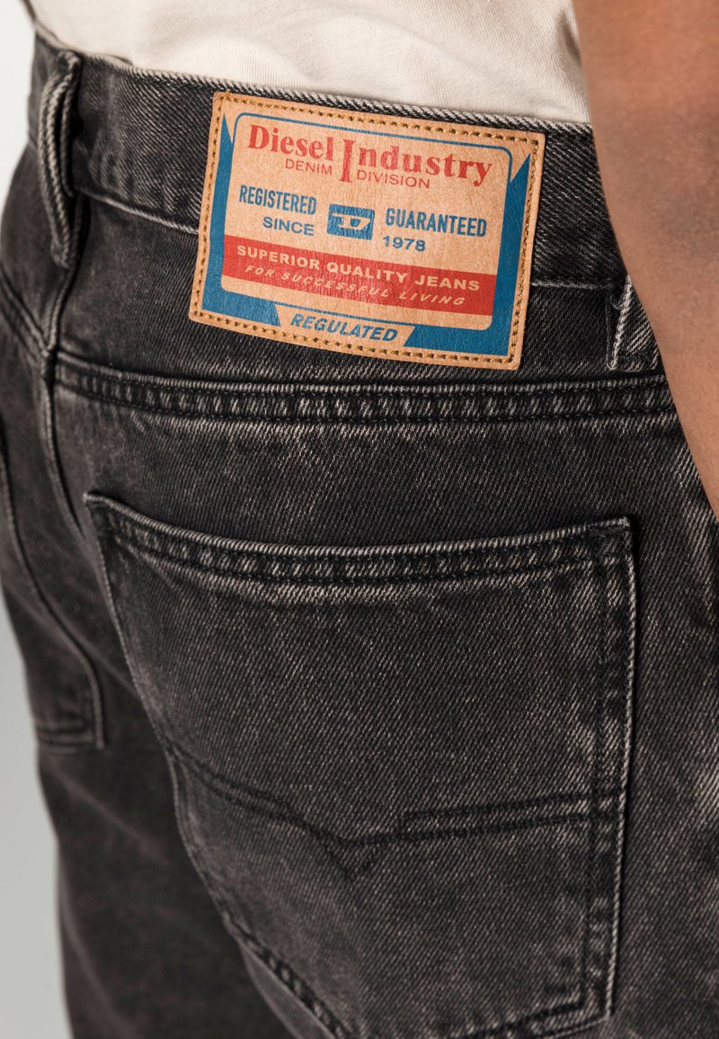 Schwarze Jeans aus Denim mit einem sichtbaren braunen Lederpatch, auf dem "Diesel Industry" steht. Die Merkmale umfassen zwei Gesäßtaschen und steppende Details.