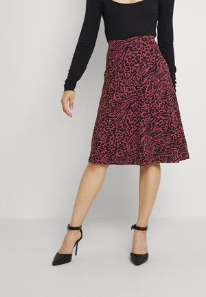 Kobieta ubrana w bordową spódnicę do kolan z czarnymi abstrakcyjnymi i panterkowymi wzorami, czarną długą bluzkę oraz czarne buty na wysokim obcasie.