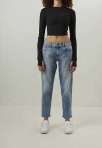Black long-sleeve crop top paired with light blue straight-leg jeans. Jeans feature a faded wash with visible stitching and pockets. White sneakers.