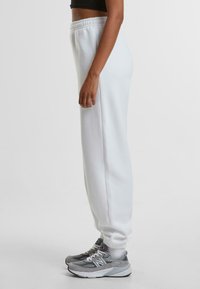 Witte sweatpants met een elastische tailleband en boorden, gemaakt van zacht materiaal. Gemaakt in combinatie met grijze sneakers met witte veters en accenten.