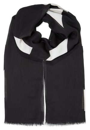Sciarpa nera con grandi motivi geometrici bianchi, tessuto leggero e bordi leggermente sfrangiati, piegata in un anello sciolto.