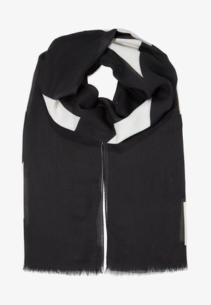 Écharpe noire avec de grands motifs géométriques blancs, tissu léger et bords légèrement effilochés, pliée en boucle lâche.