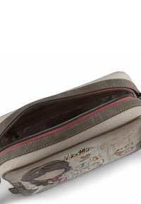 Graue und cremefarbene Tasche aus synthetischem Leder mit dekorativer Illustration, goldenen Akzenten, rotem Reißverschluss und gemustertem Innenfutter.