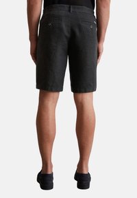Dunkelgraue Leinen Shorts im entspannten Schnitt, mit zwei hinteren Taschen mit Knöpfen und einem schlichten Bund. Getragen mit schwarzen Schuhen.
