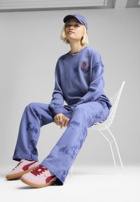 Violeta krāsu diegs svītru krekls ar sarkanu izšuvumu, atbilstošas violeta krāsa bikses un rozā kedas ar sarkaniem akcentiem. Valkāts ar violetu cepuri.