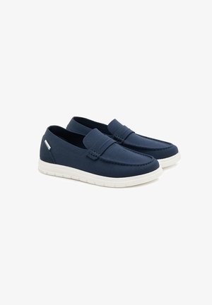 Paar marineblauwe casual slip-on loafers met gestructureerde stof en witte rubberen zolen op een witte achtergrond.