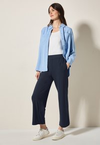 Lichtblauwe button-up shirt, witte tanktop, marineblauwe cropped broek en witte sneakers. Zachte stof en relaxte pasvorm met elastische tailleband.