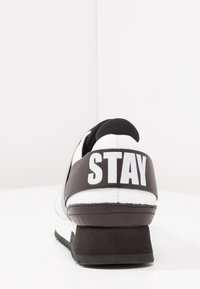Svart och vit sneakers med en texturerad läderöverkonstruktion, en kraftig klack och en framträdande "STAY" grafik på hälkappan.
