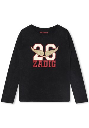 Czarna koszula z długim rękawem z dużą białą cyfrą „26” obrysowaną na czerwono, złotymi brokatowymi skrzydłami na liczbach oraz czerwonym napisem „ZADIG” poniżej.