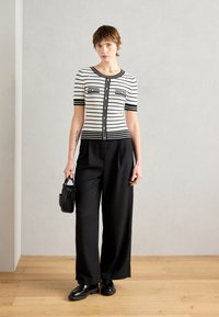 Haut à manches courtes rayé noir et blanc avec deux poches avant, pantalons larges noirs, sac noir et chaussures noires brillantes.