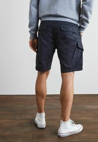 Marinefarbene Cargo-Shorts mit mehreren Taschen, aus strapazierfähigem Stoff. Getragen mit weißen Sneakers, der einen lässigen, entspannten Stil zeigt.
