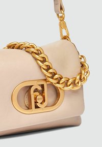 Sac à main en cuir beige clair avec une grande sangle en chaîne dorée et un fermoir logo doré proéminent au design ovale.