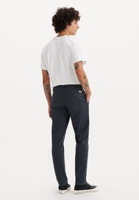 Mørkegrå bomuldsbukser med lige snit, der har baglommer og minimal branding. Båret med en enkel hvid t-shirt og sorte sneakers.