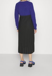 Maglione a maglia viola, gonna midi plissettata nera e sandali blu con cinturini e tacchi spessi. Tessuto liscio e dettagli in maglia testurizzati.