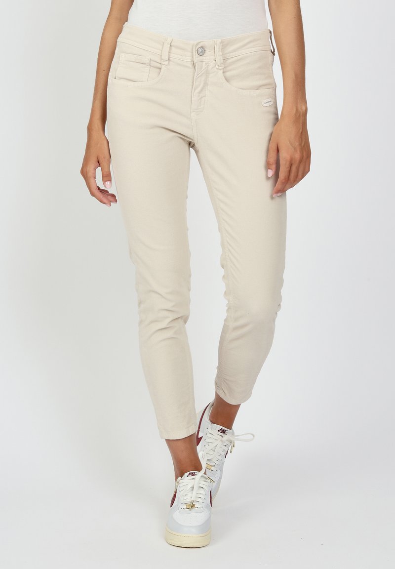 Beige slim-fit pants with a ribbed texture and front pockets, paired with white sneakers and visible laces, showcasing casual style.