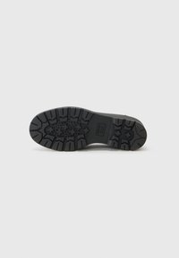 Semelle de chaussure en caoutchouc noir avec des motifs de crantage profonds, comportant des découpes circulaires et une surface texturée pour une meilleure adhérence. Marque Geox visible.
