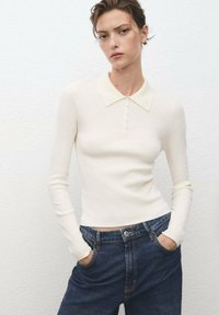Pull en tricot côtelé de couleur crème avec un col net et une patte de boutonnage, associé à un jean denim foncé taille haute.