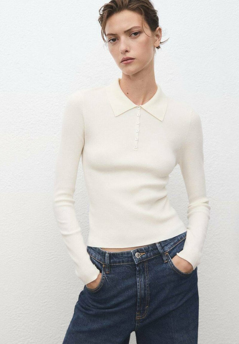 Pull en tricot côtelé de couleur crème avec un col net et une patte de boutonnage, associé à un jean denim foncé taille haute.
