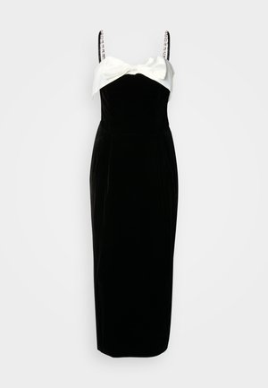 Crna baršunasta haljina s bijelim satenskim mašnom na izrezu, koja ima tanke naramenice i uski kroj s midi dužinom.