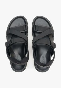 Zwarte sandalen met elastische banden en een platte zool. Ontworpen met een minimalistische esthetiek en verstelbare sluitingen voor een veilige pasvorm.