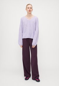 Lys lilla strikket genser med V-hals og litt cropped passform, kombinert med høy midje mørk lilla vide bukser og svarte joggesko.