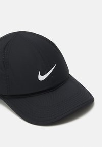 Juodas Nike kepurė su išlenktu kraštu ir balta logotipu. Pagaminta iš lygaus, lengvo audinio, šonuose su ventiliacijos detalėmis.
