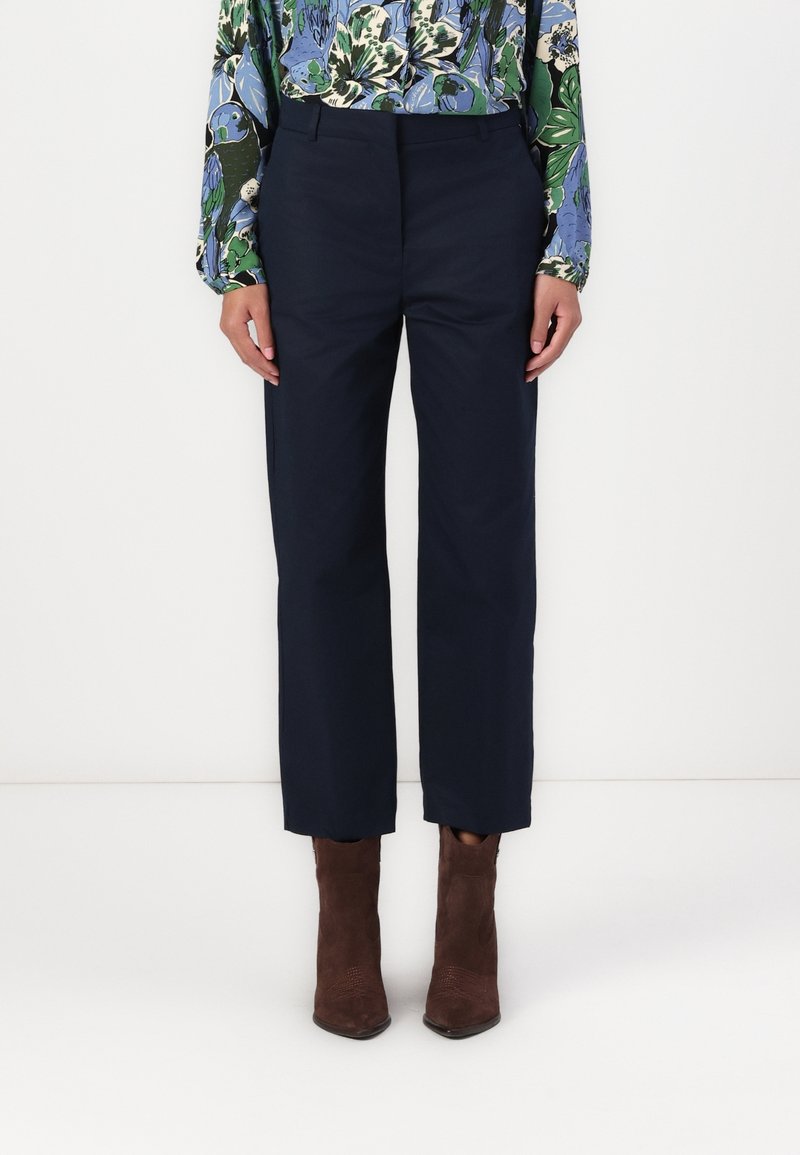 Marineblauwe broek met een rechte snit, met een gladde textuur en een voorplooien, gecombineerd met bruine leren enkellaarsjes.