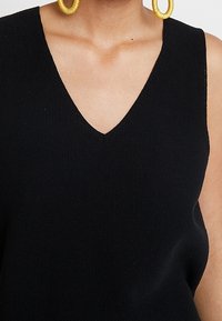 Czarny dziergany top bez rękawów z dekoltem w serek i teksturowaną tkaniną. Charakteryzuje się widocznym przeszyciem i luźnym krojem.