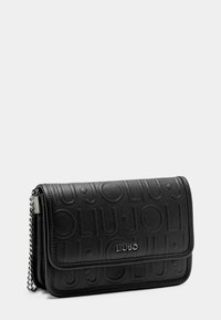 Cartera de piel sintética negra con patrón de logo embosado, herrajes plateados y correa de cadena, con cierre de solapa y diseño compacto.