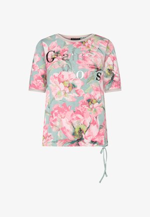 Kortærmet skjorte med stort lyserødt blomstermønster på lysblå baggrund og dekorativ tekst "Glamorous" på forsiden, bindedetalje nederst.