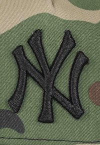 Baseball cap featuring a camo pattern with olive green and tan shades. Black embroidered "NY" logo prominently displayed in the center.